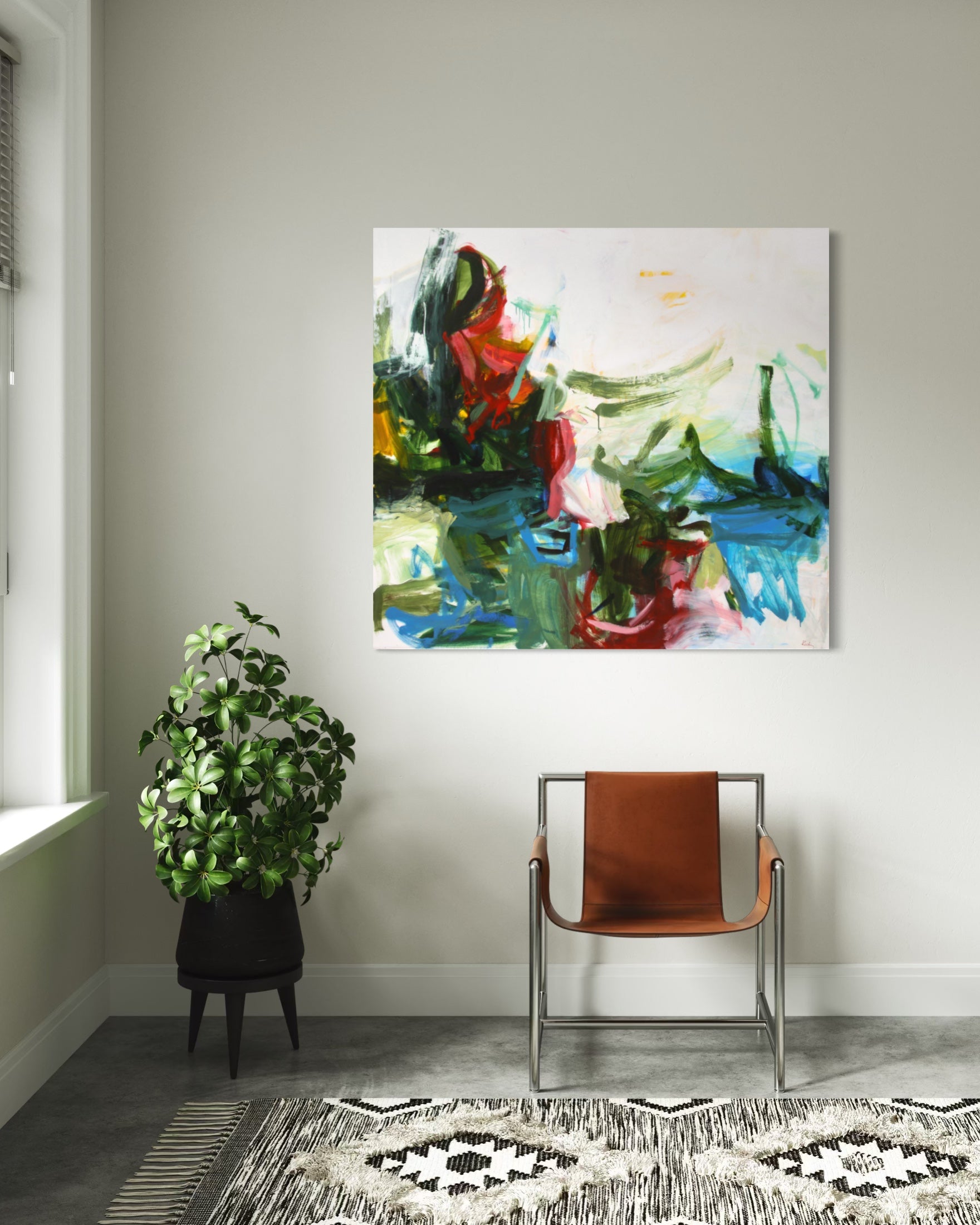 An abstract canvas painting with vibrant green, blue, red, and white brushstrokes, displayed on a light gray wall in a modern room setting above a brown leather chair and a patterned rug.