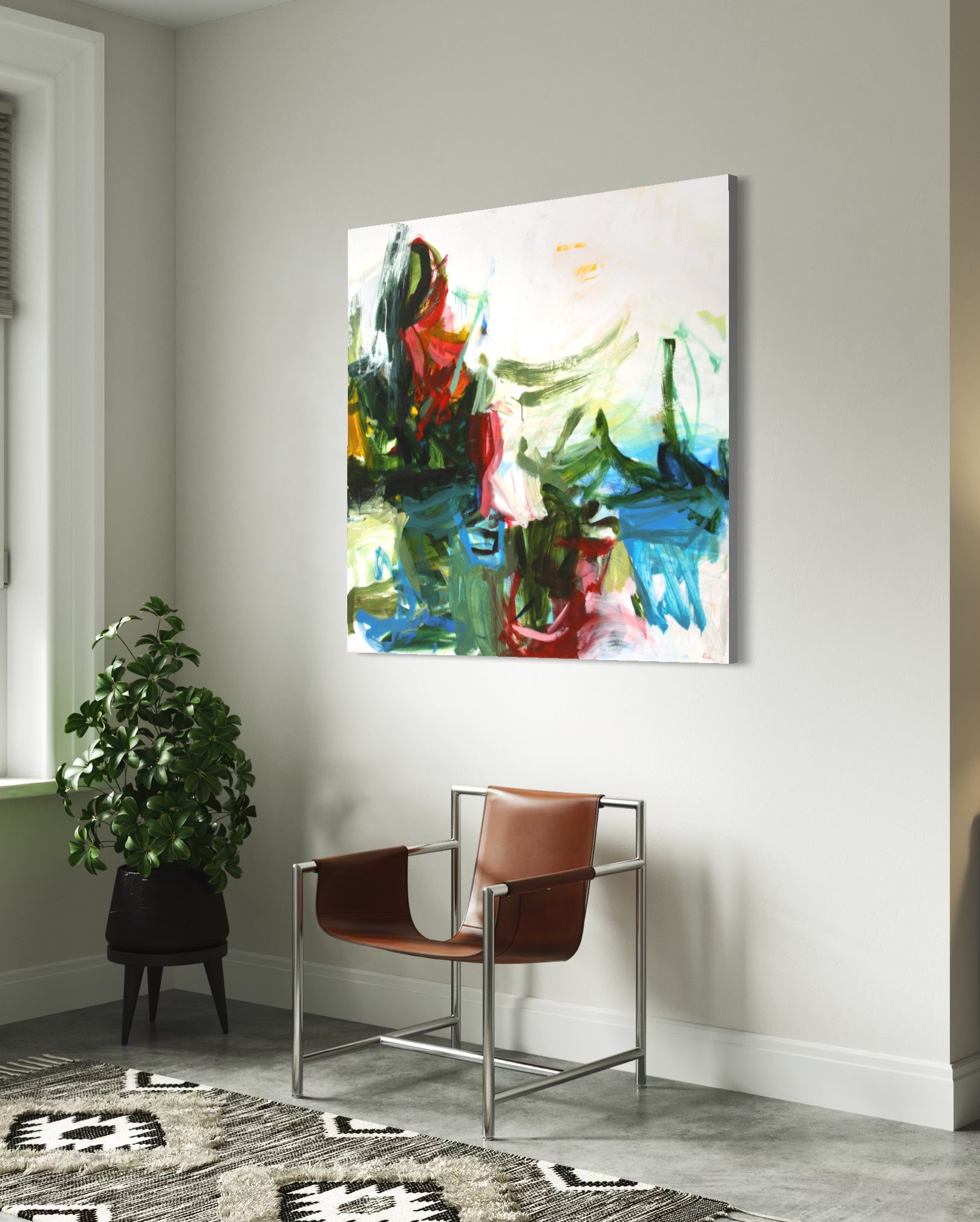 Abstract canvas wall art with expressive brushstrokes in green, blue, red, white, and yellow, displayed in a modern living room setting above a brown leather chair and next to a potted plant.