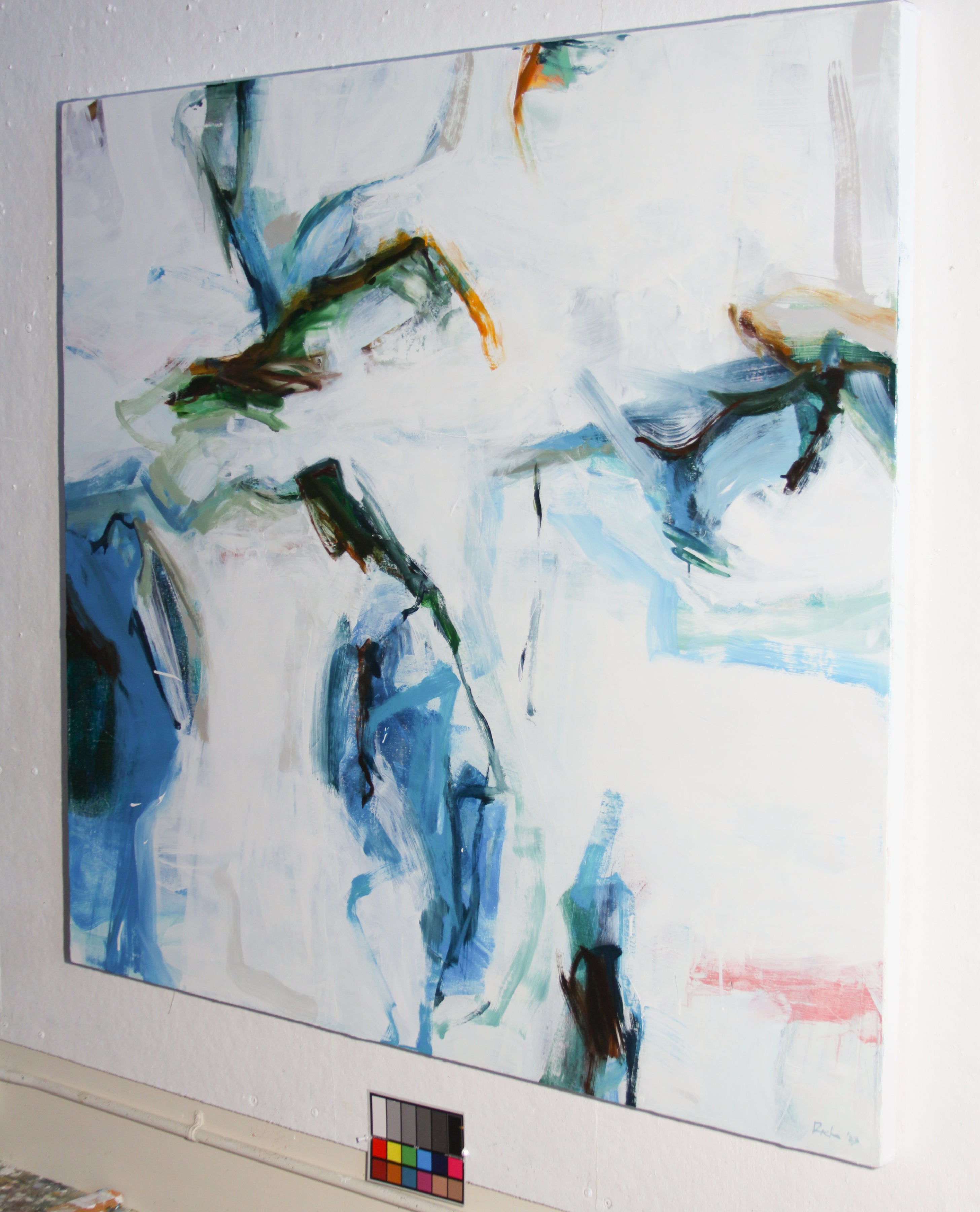 An abstract canvas painting with expressive brushstrokes in shades of blue, green, black, and touches of orange and pink on a white background, displayed on a gallery wall with a color card below it.