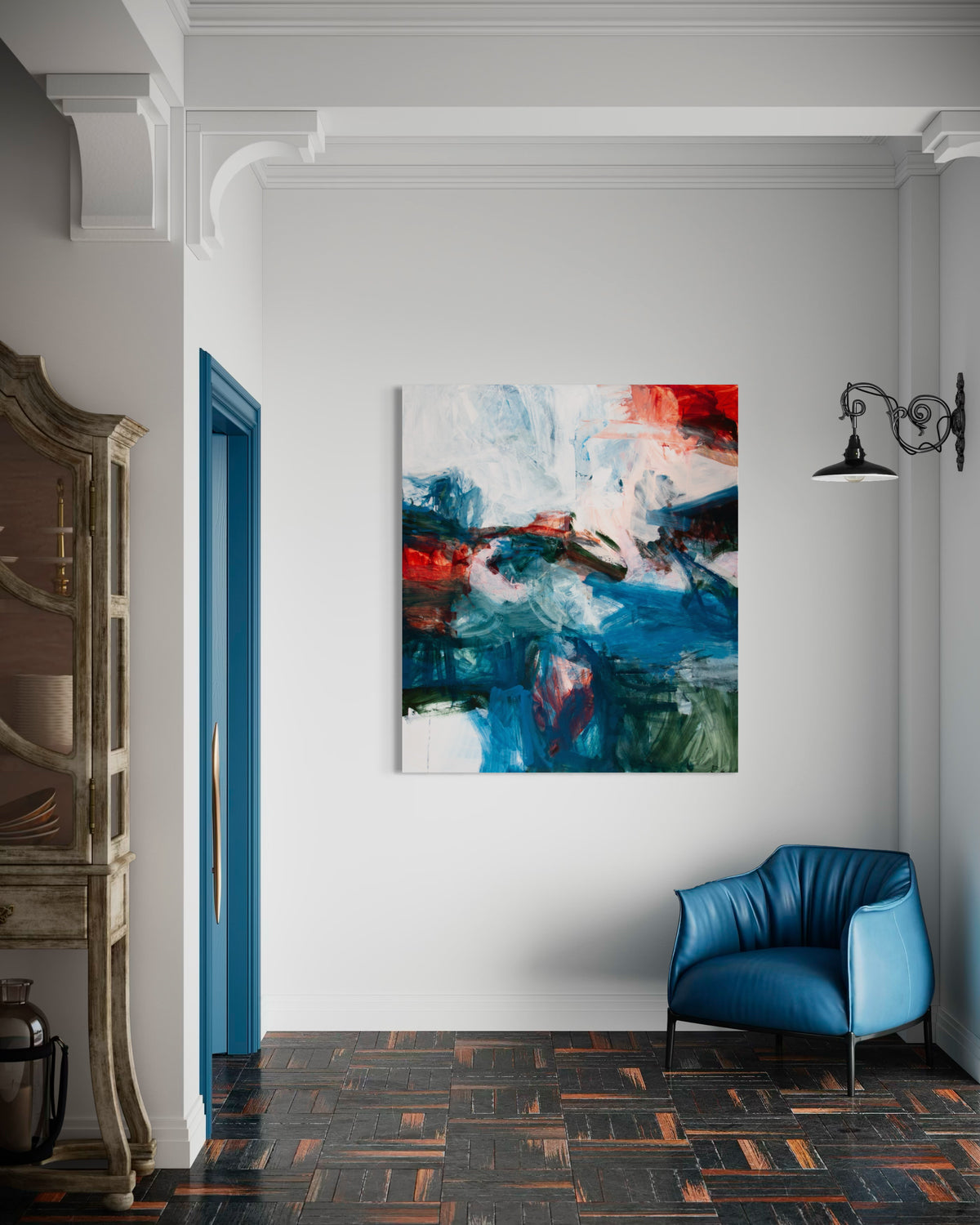 An abstract canvas painting by Michael Rich with blue, red, white, and green brushstrokes hanging on a white wall in a modern room with a blue armchair and patterned wood floor.