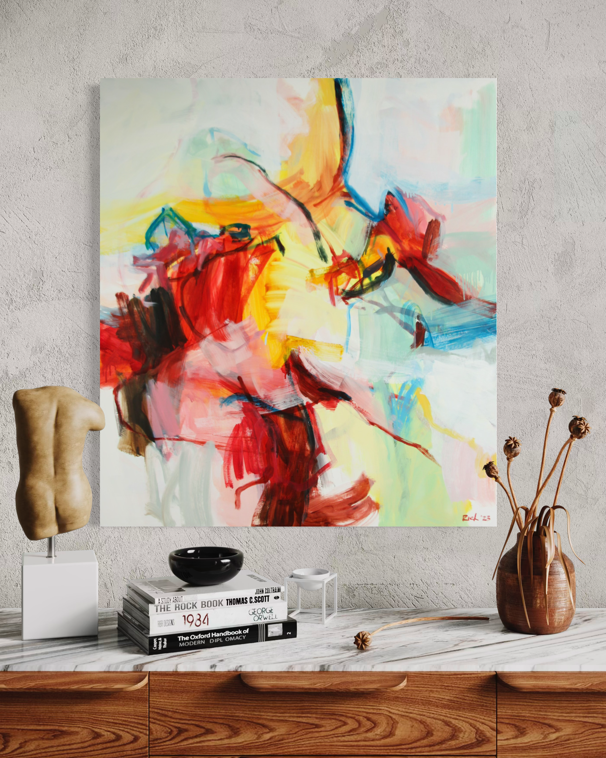 An abstract canvas painting with vibrant red, yellow, blue, and green brushstrokes on a white background, displayed on a gray textured wall above a marble-topped console table with decorative objects.