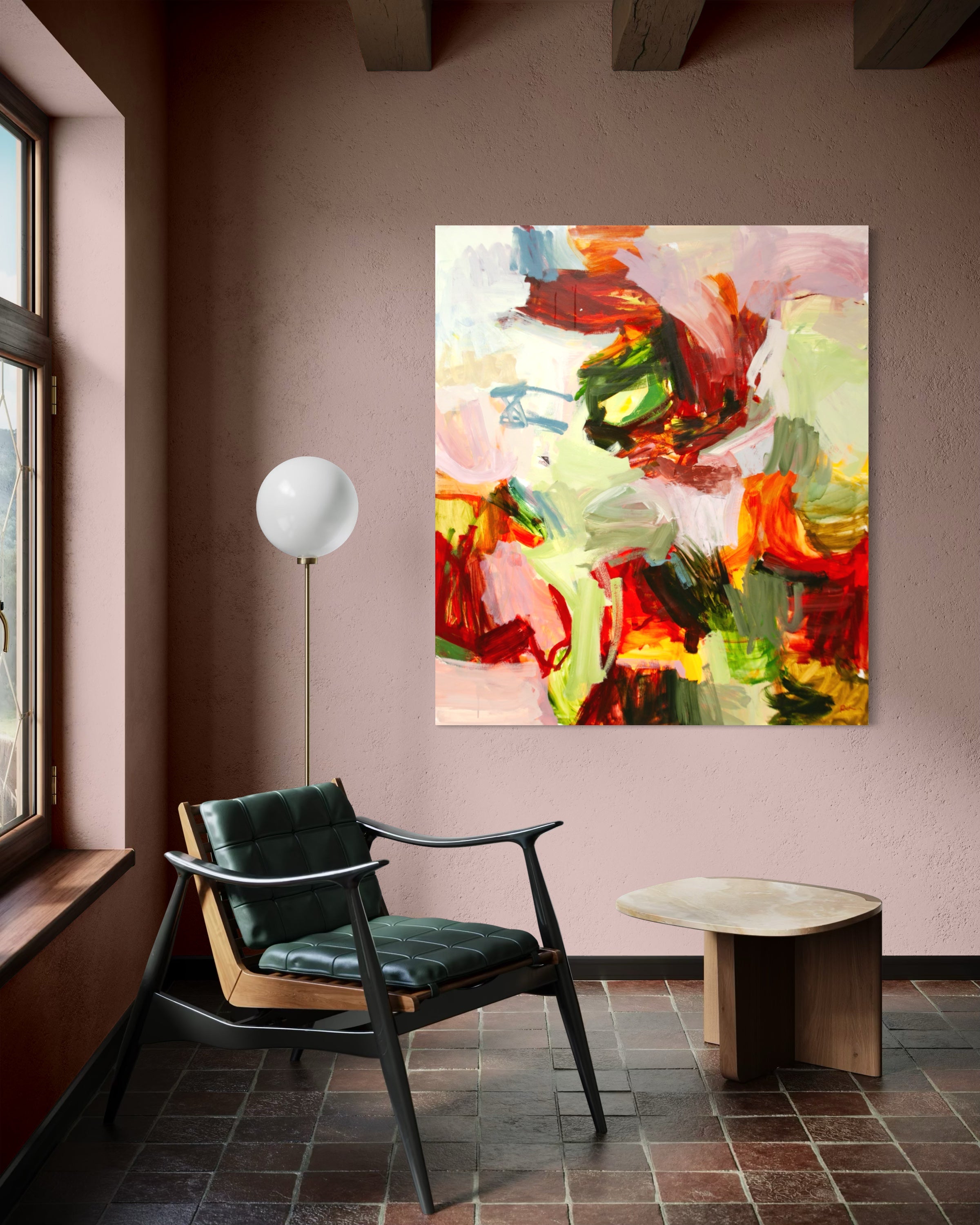 An abstract canvas painting with vibrant red, green, yellow, and white brushstrokes hanging on a dusty rose wall in a modern room setting with a black leather armchair, a small wooden side table, and a white globe floor lamp.