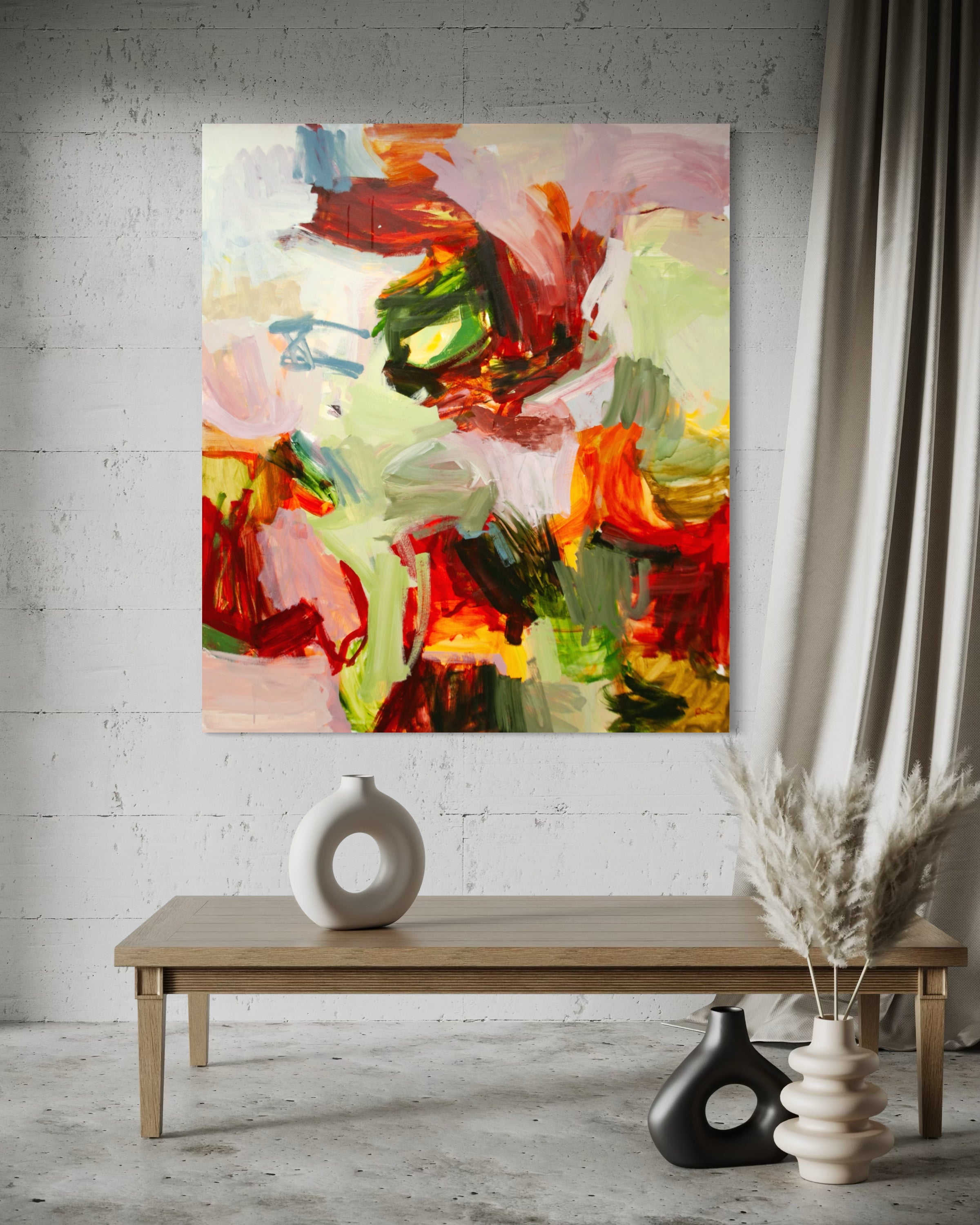 An abstract canvas painting with expressive brushstrokes in red, green, yellow, pink, and white, displayed on a white brick wall above a wooden table with decorative vases.