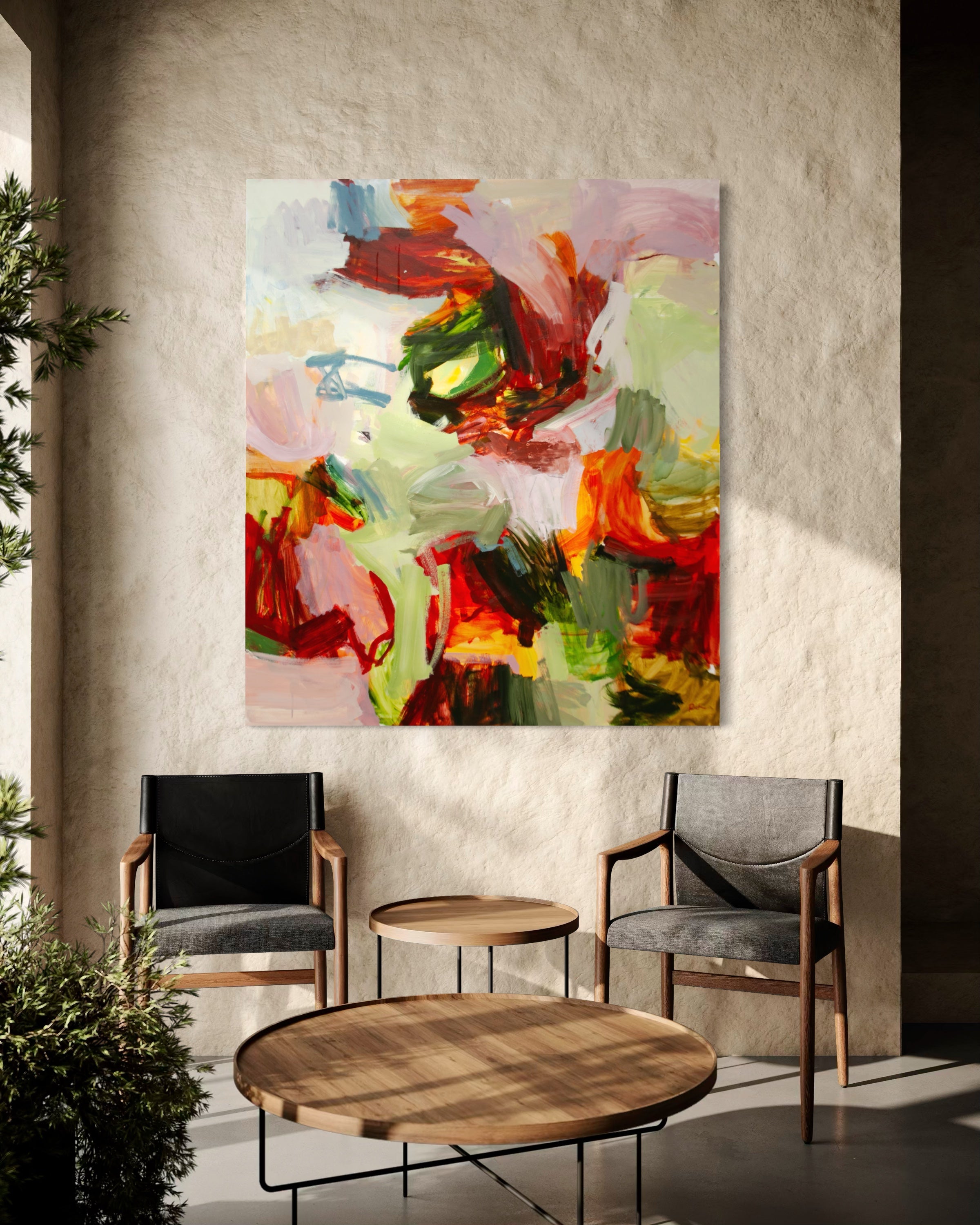 An abstract canvas painting with vibrant red, green, yellow, pink, and blue brushstrokes hanging on a textured beige wall in a modern living room setting with two armchairs and a round wooden coffee table.