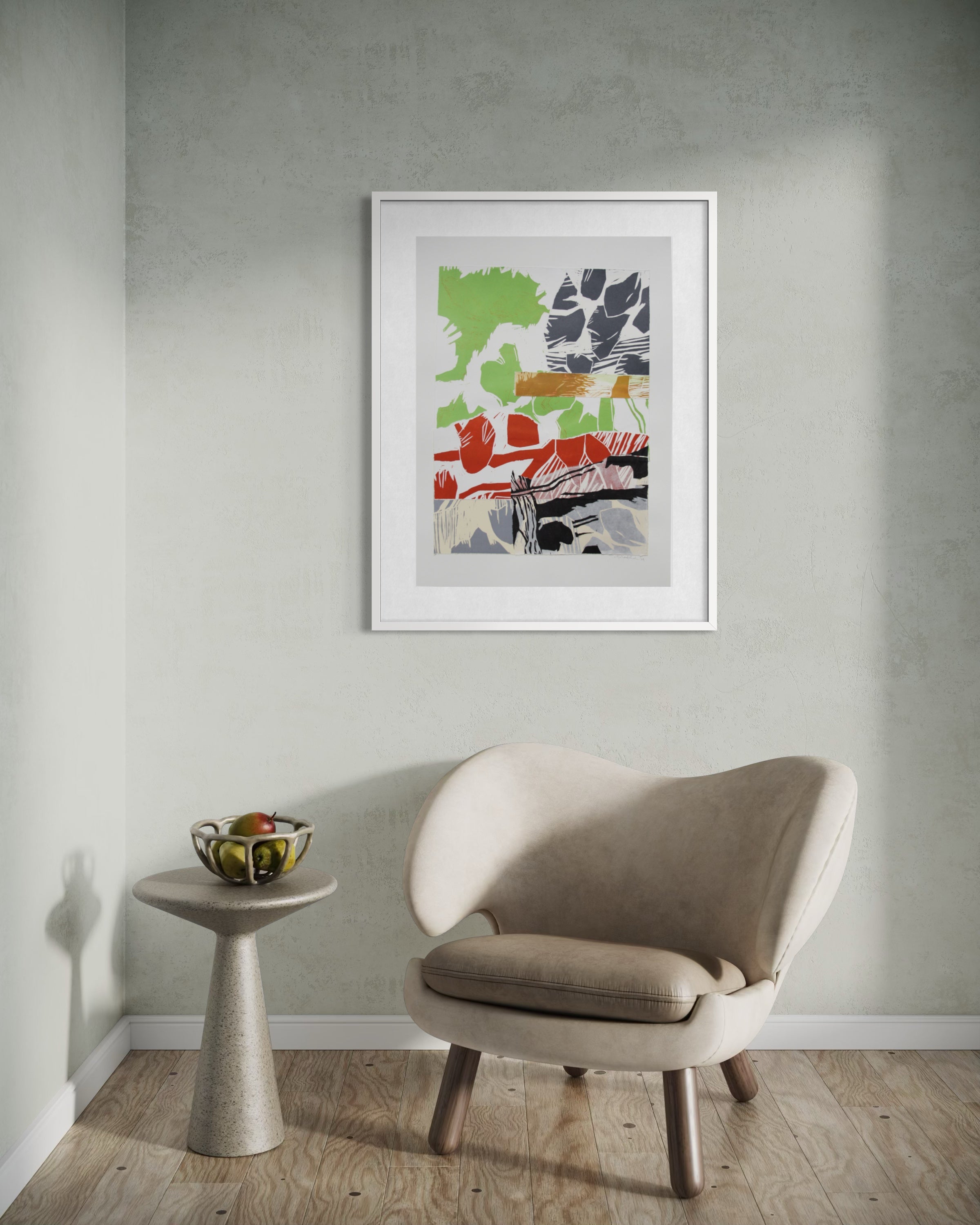 A framed abstract art print hangs on a textured light gray wall above a beige armchair and a small round side table with a bowl of fruit.