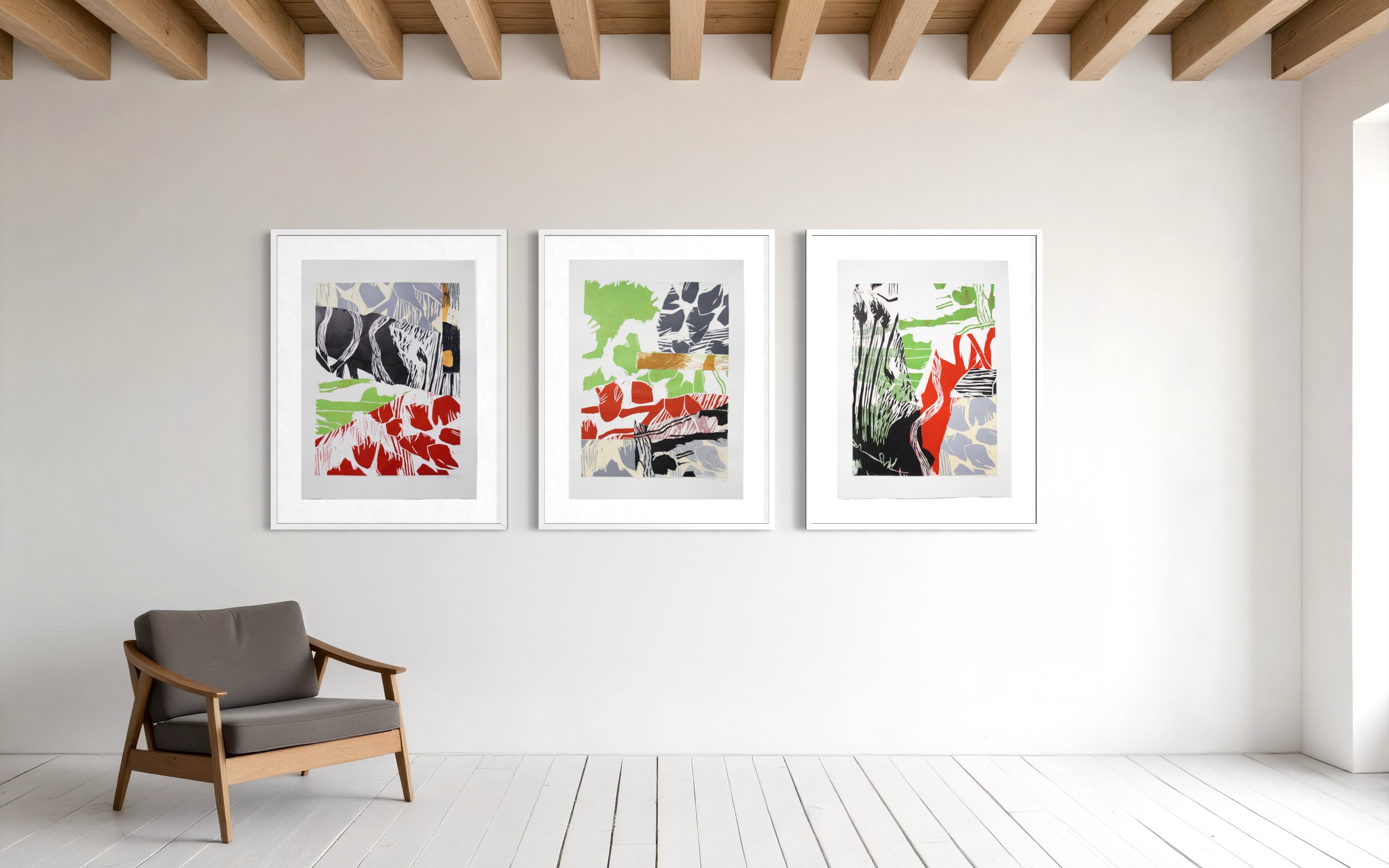Three framed abstract art prints with white frames are displayed on a white wall in a bright room with light wood ceiling beams and a gray armchair.