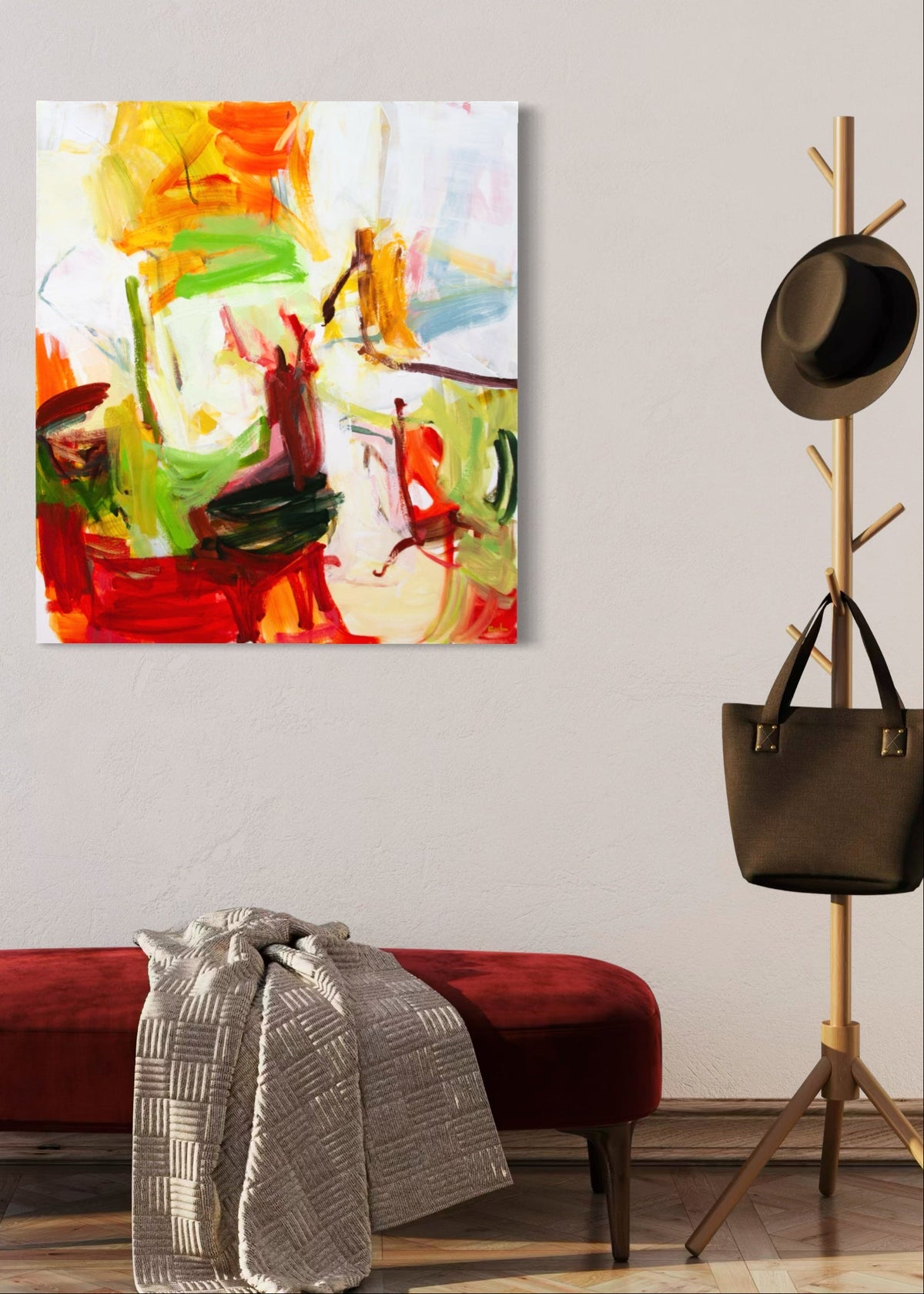 An abstract canvas painting by Michael Rich with vibrant brushstrokes of red, green, yellow, orange, and white, displayed on a light gray wall above a red velvet bench with a gray throw blanket.