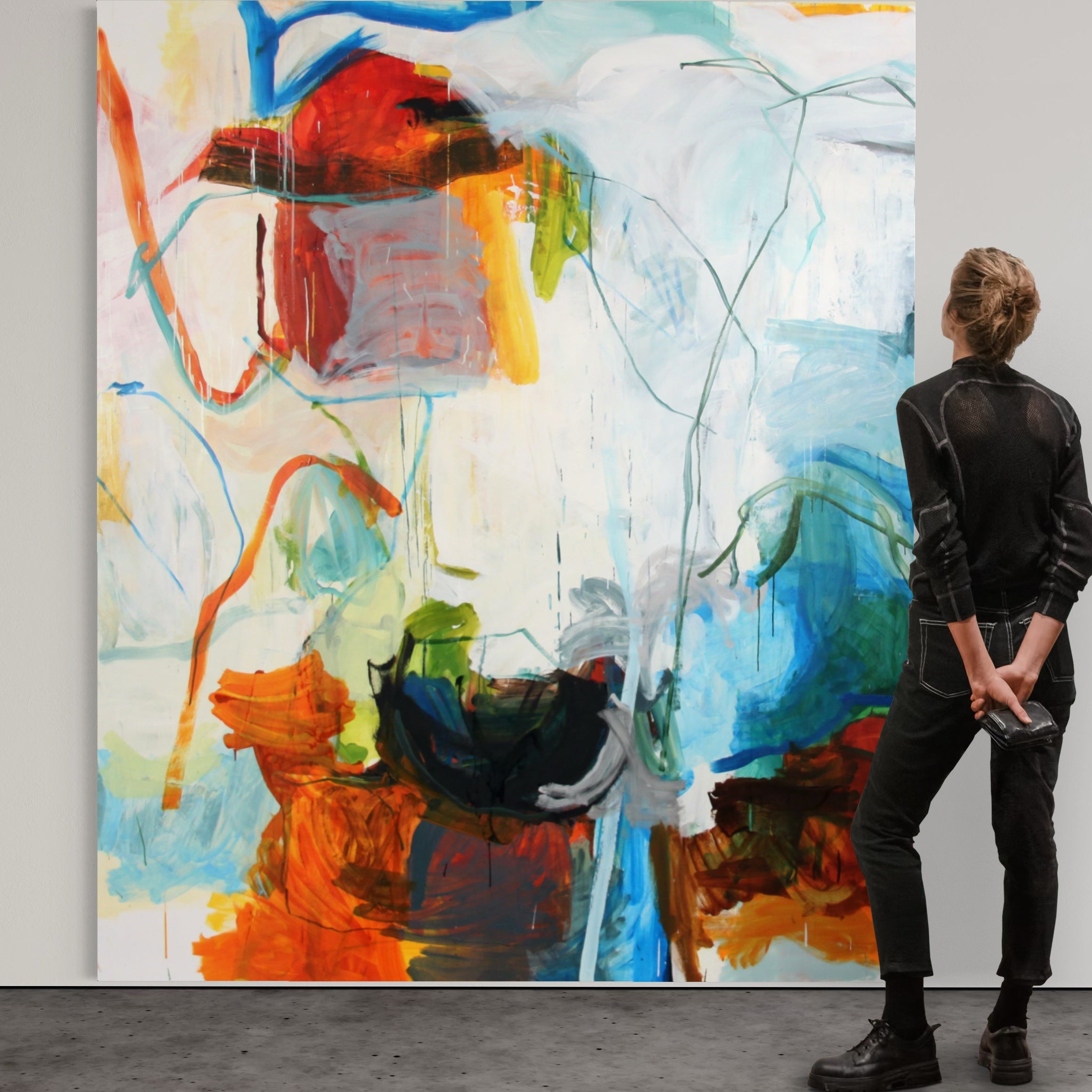 A person in a black outfit stands in profile facing a large abstract canvas painting with bold brushstrokes in blue, white, orange, red, green, and black.