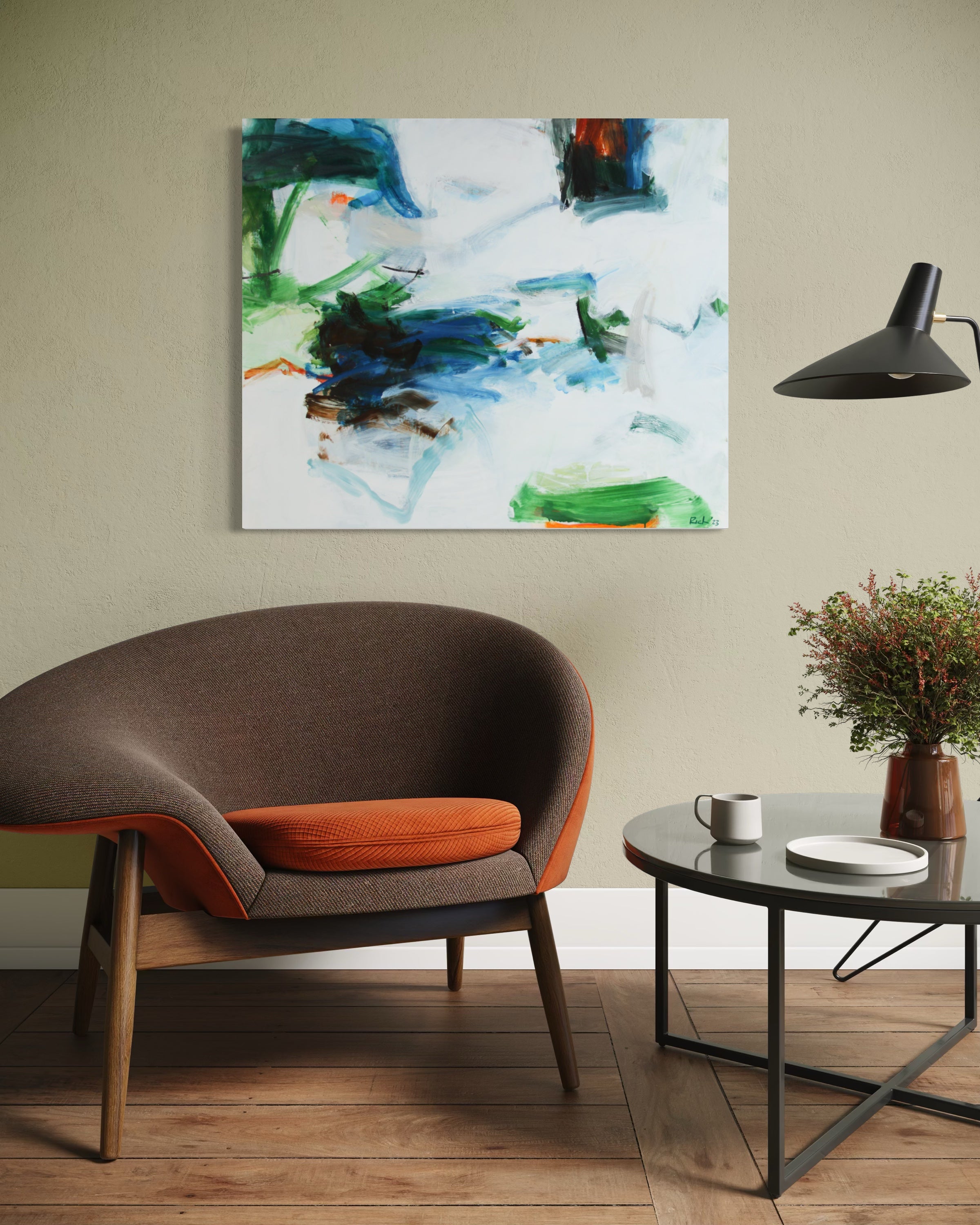 An abstract painting by Michael Rich with blue, green, and white brushstrokes hanging on a beige wall in a modern living room setting with a brown armchair, side table, and lamp.