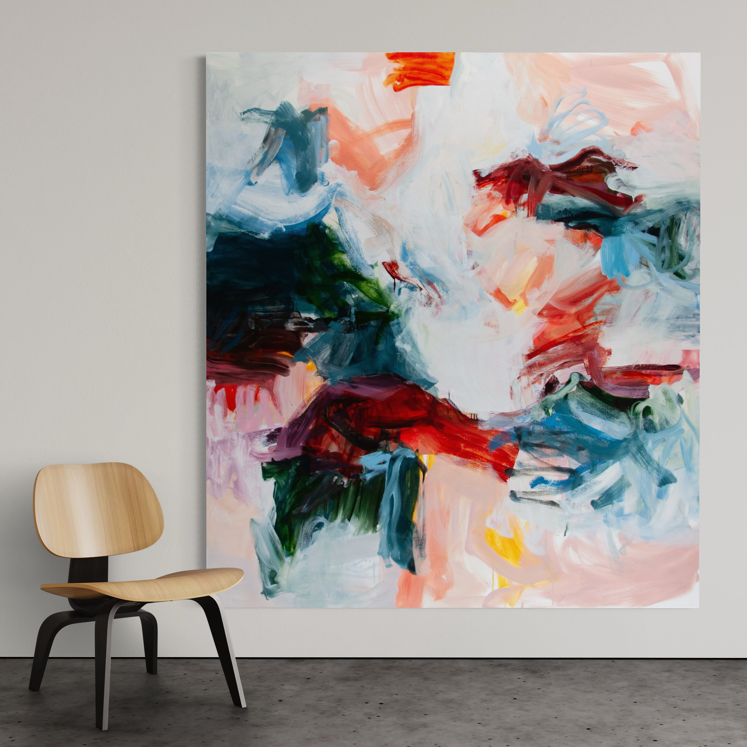 An abstract canvas painting with expressive brushstrokes in white, blue, pink, red, green, and orange, displayed on a light gray wall next to a modern wooden chair.