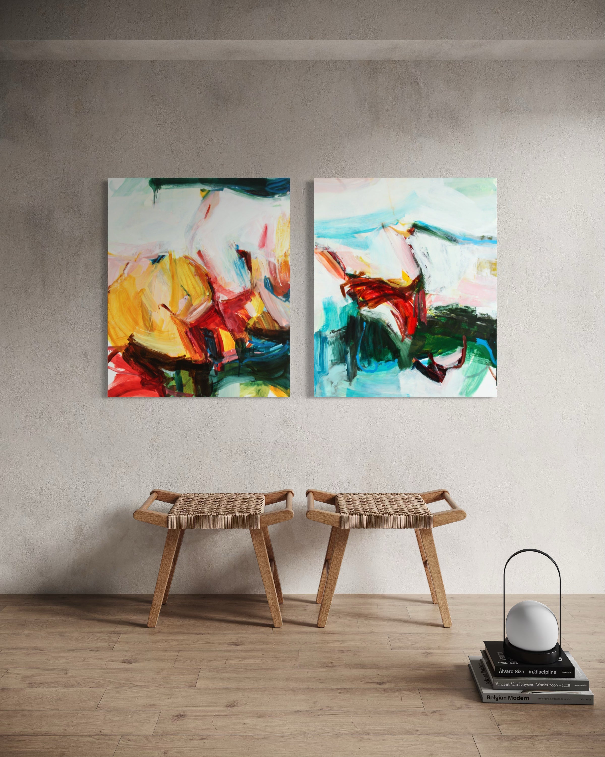 Two abstract canvas wall art prints hanging side by side on a textured light gray wall above two woven wooden stools in a minimalist room setting.