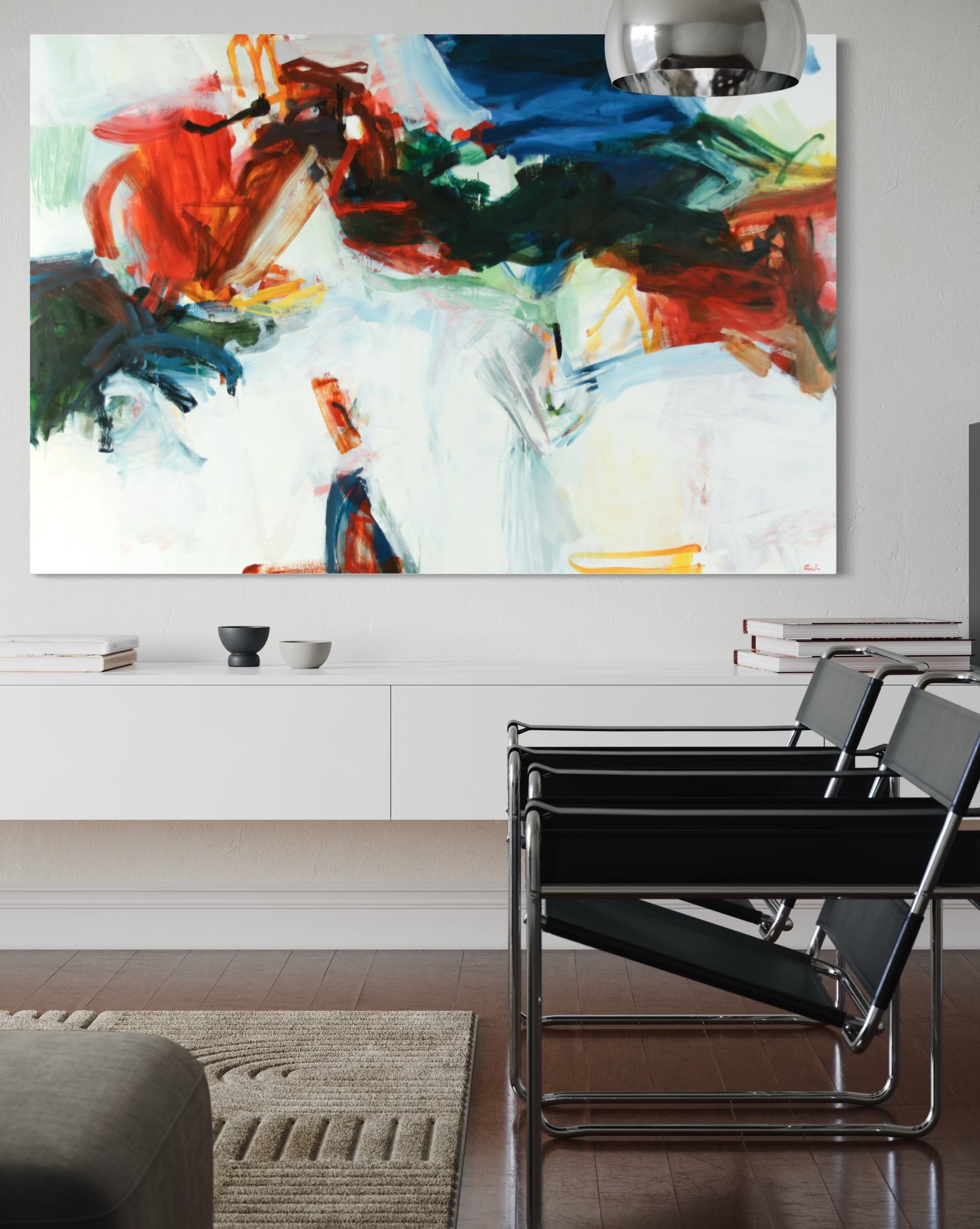 A large abstract canvas wall art print with bold brushstrokes of red, blue, green, black, and white, displayed in a modern living room setting above a white wall cabinet and black chairs.