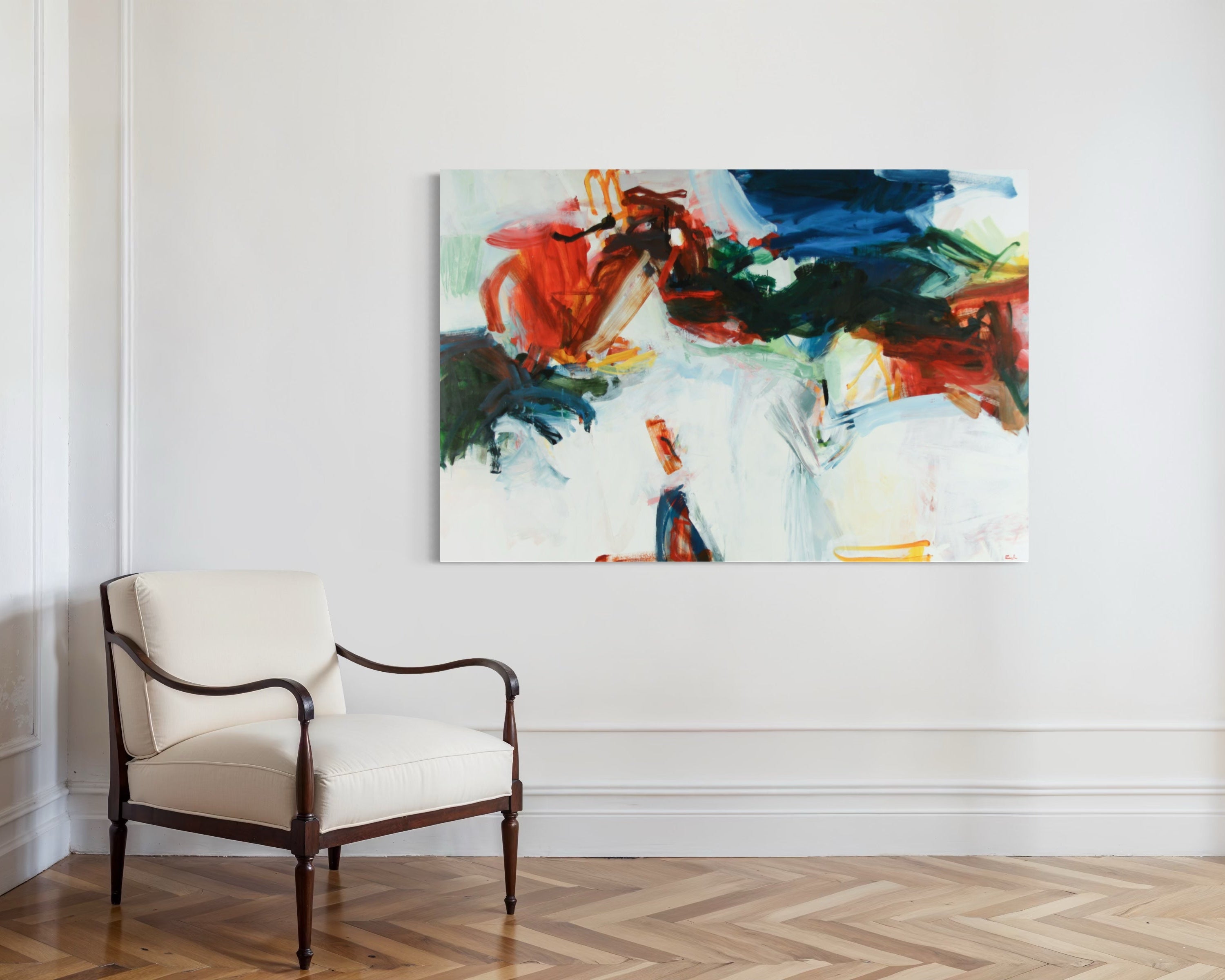 An abstract canvas painting with vibrant red, blue, green, and white brushstrokes, displayed on a white wall in a modern room with a cream-colored armchair and a light wood herringbone floor.
