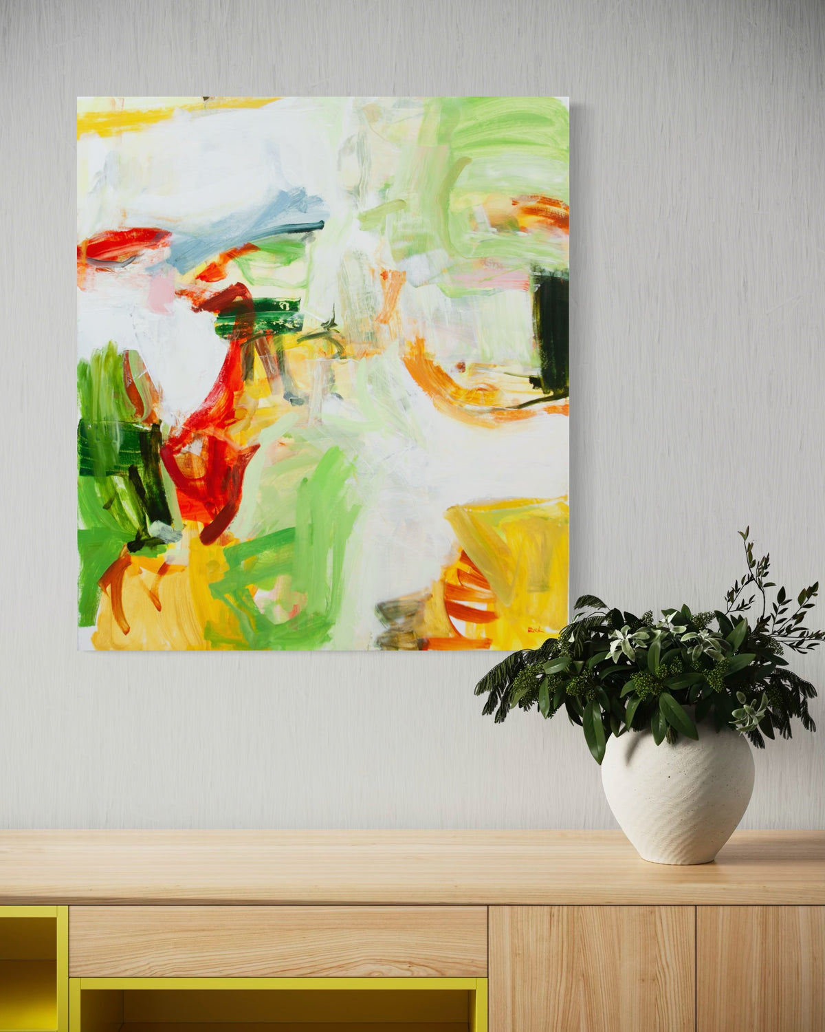 Abstract painting by Michael Rich with expressive green, yellow, red, orange, and white brushstrokes, displayed on a light gray wall above a wooden console table with a potted green plant in a white vase.