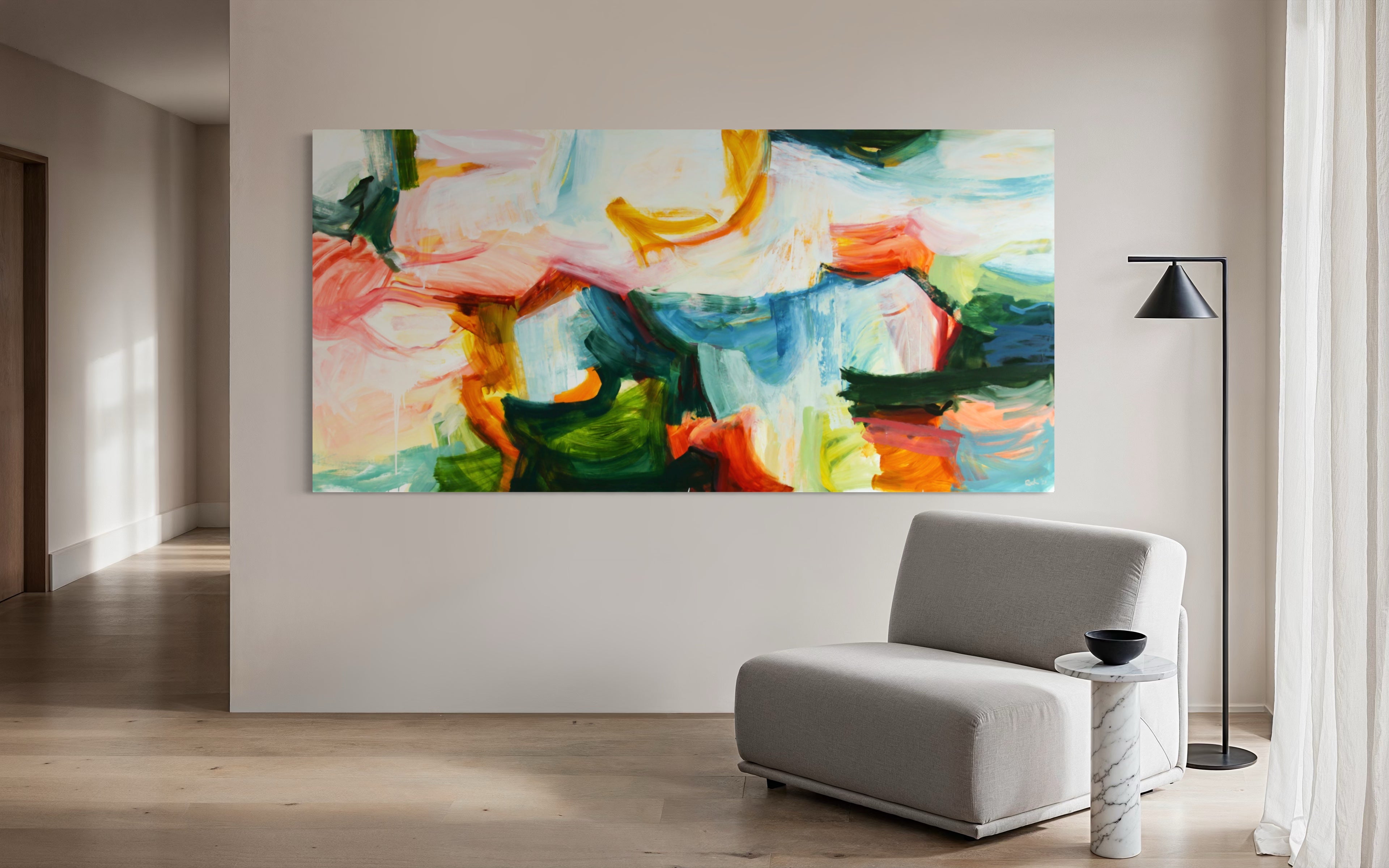 A large abstract canvas painting with vibrant green, blue, orange, pink, and white brushstrokes, displayed on a light beige wall in a modern living room setting with a gray armchair and a black floor lamp.