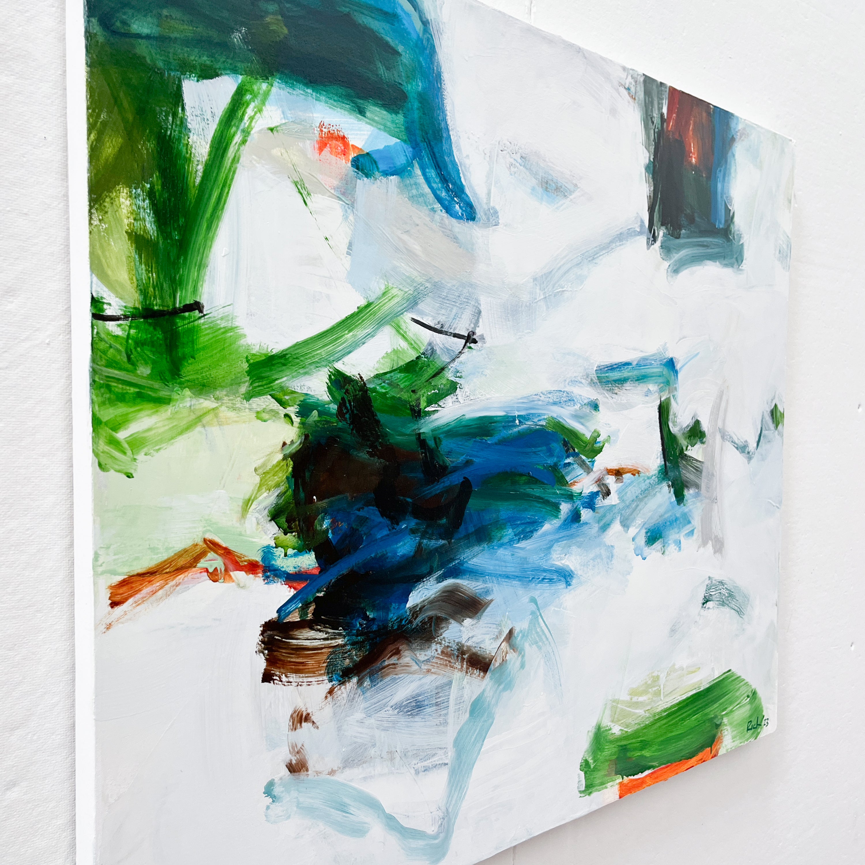 An abstract canvas painting with expressive brushstrokes in green, blue, white, black, and touches of orange, shown hanging on a white wall.