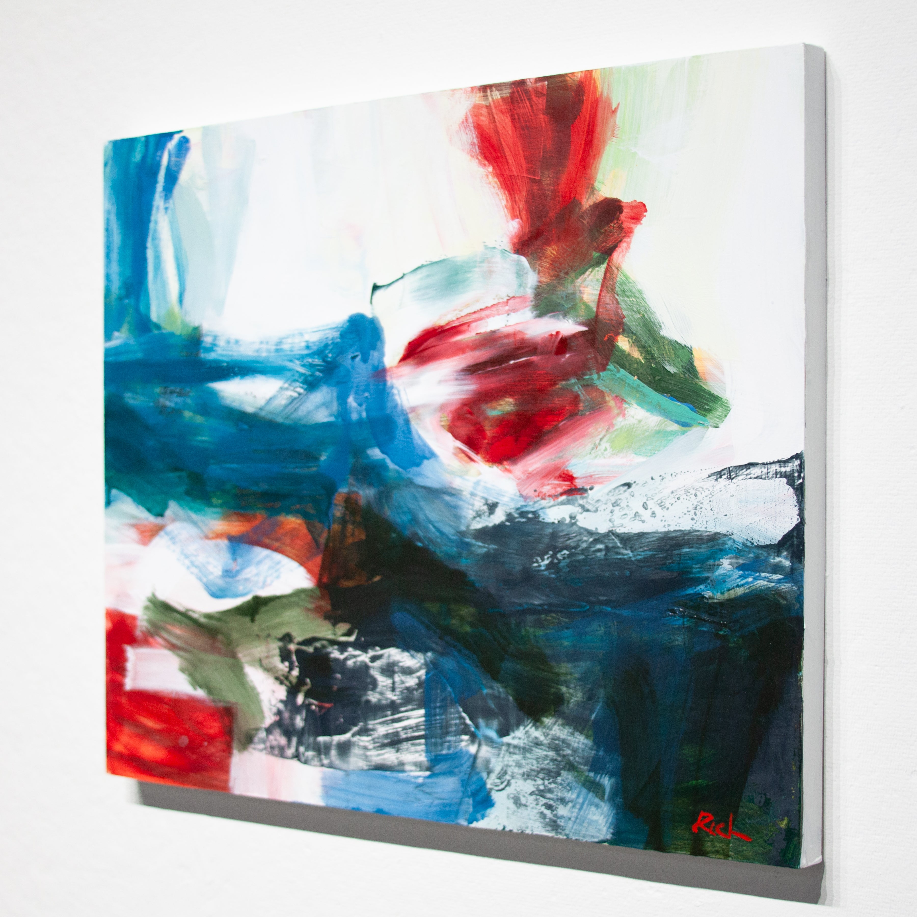 Abstract canvas wall art featuring expressive brushstrokes in blue, red, green, white, and black, shown hanging on a light gray wall.
