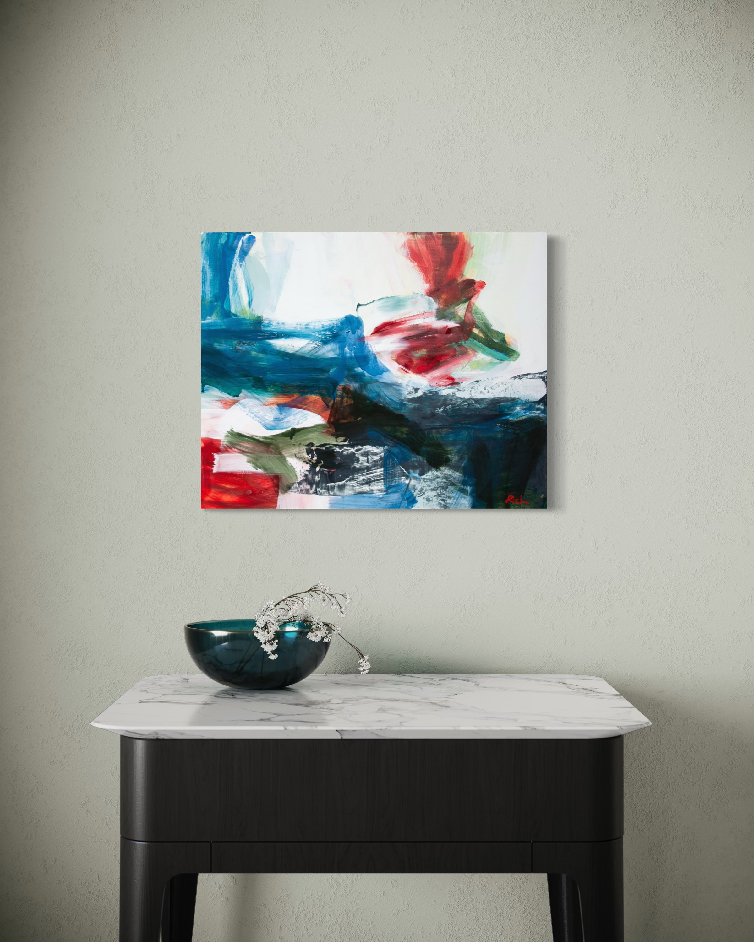 Abstract canvas wall art featuring bold blue, red, white, and black brushstrokes, displayed on a light gray wall above a dark console table with a marble top and a decorative bowl.
